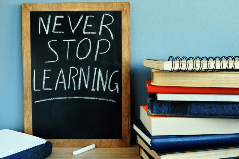 Books next to a blackboard on which it is written that you should never stop learning.