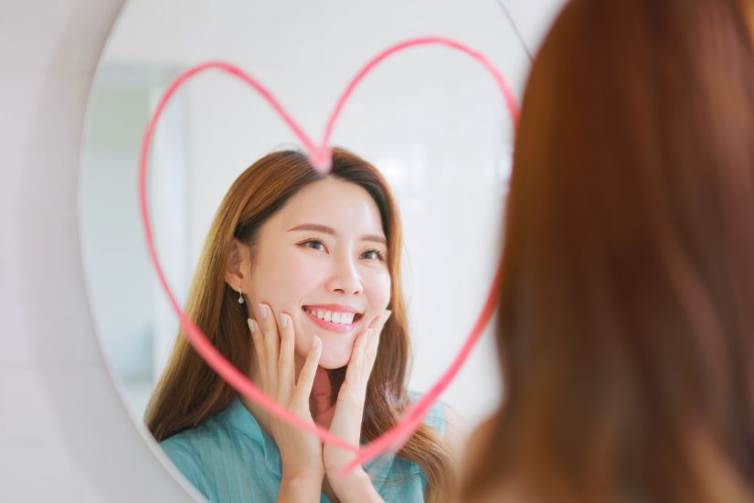 Celebrating achievements and rewarding yourself when setting goals. A woman looking at a heart drawn on a mirror.