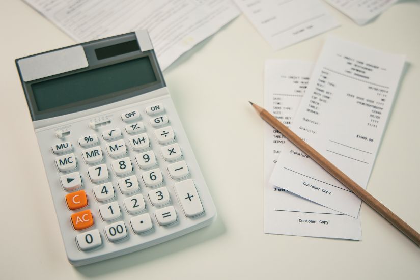 List Your Expenses to make a real budget.  A calculator and pencil next to papers and receipts.