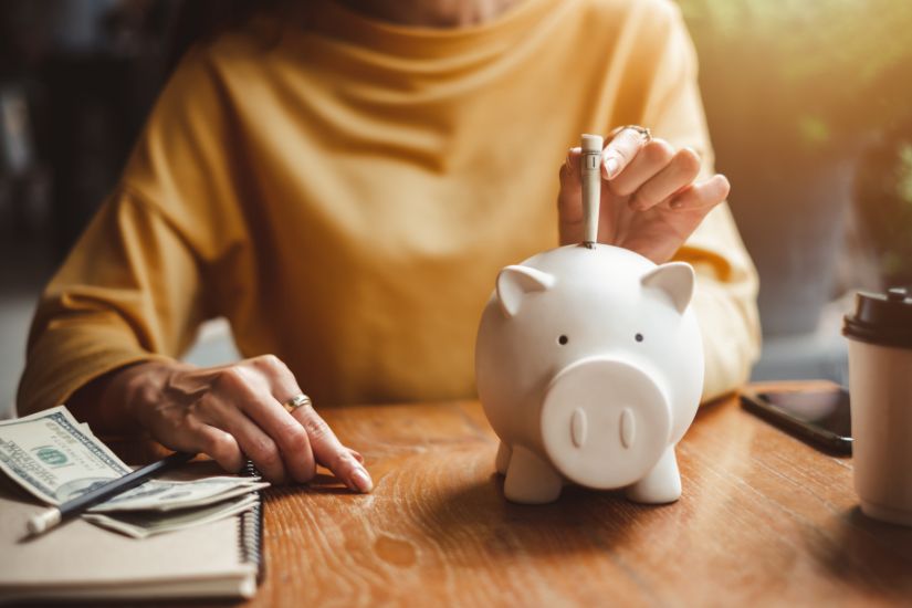 To ensure your financial foundation is secure, it’s important to review both your savings and long-term investments. A woman saving in a piggy bank.